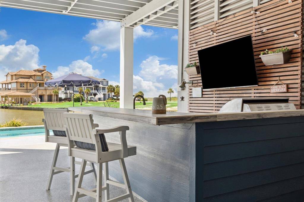 The ground level living space includes a built-in bar area with a TV, under-counter appliances, and bar seating, perfect for watching the game or hosting friends poolside