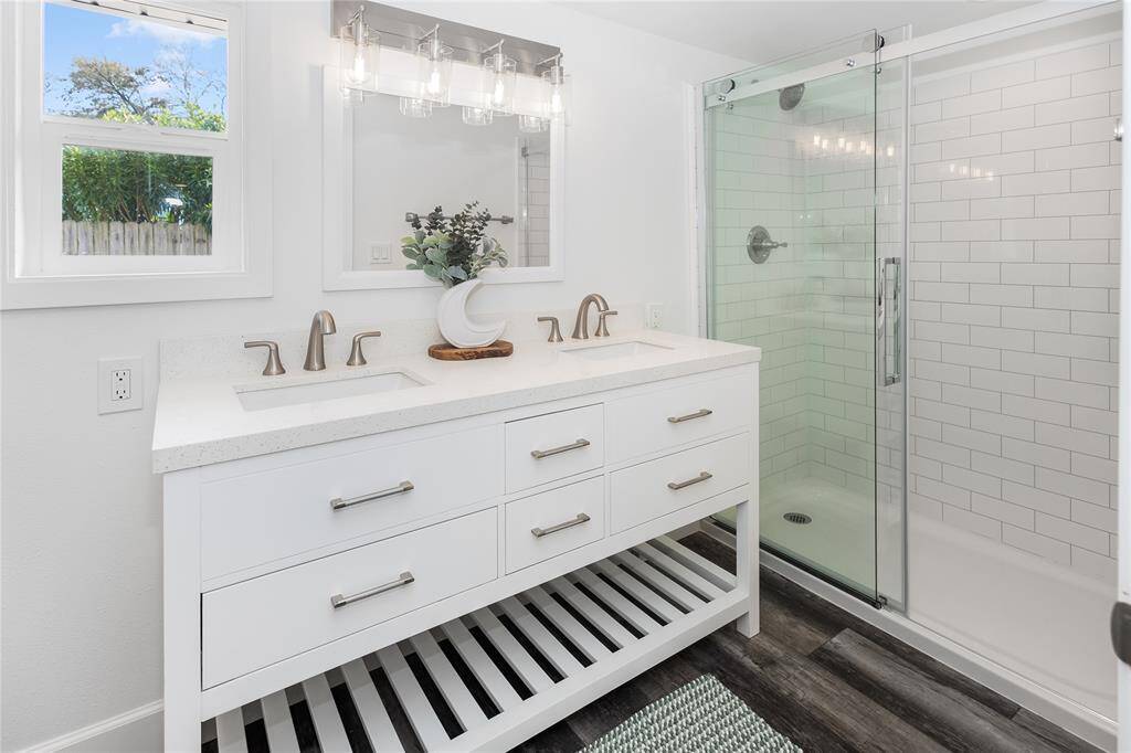 A sleek vanity mirror, double sinks, elegant lighting, and a spacious glass-enclosed shower create a spa-like retreat.
