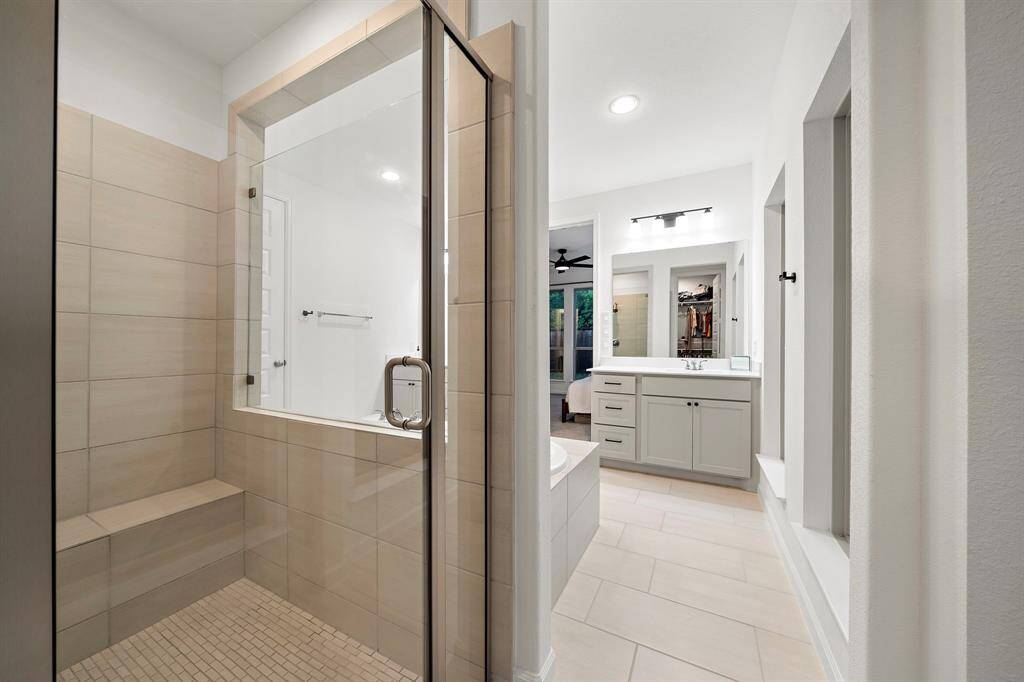 The walk-in shower has tile surround, sitting area, and glass door.