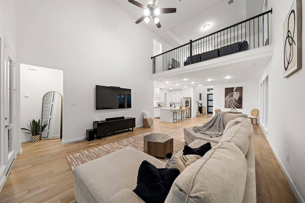 Living room features beautiful flooring, aceiling fan, high ceilings, and large windows.