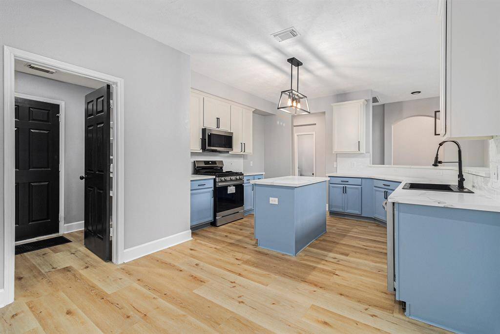 This modern kitchen features a stylish design with light blue cabinetry, a central island, and stainless steel appliances. It has a sleek black faucet and ample lighting, creating a bright and inviting space.