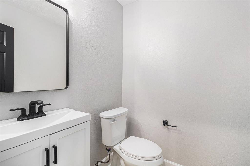 This photo shows a half bathroom with a white vanity and sink, black fixtures, and a simple toilet.