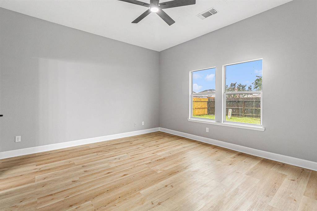 The downstairs primary bedroom features two large windows providing ample natural light. A modern ceiling fan is installed, and the space feels bright and airy.