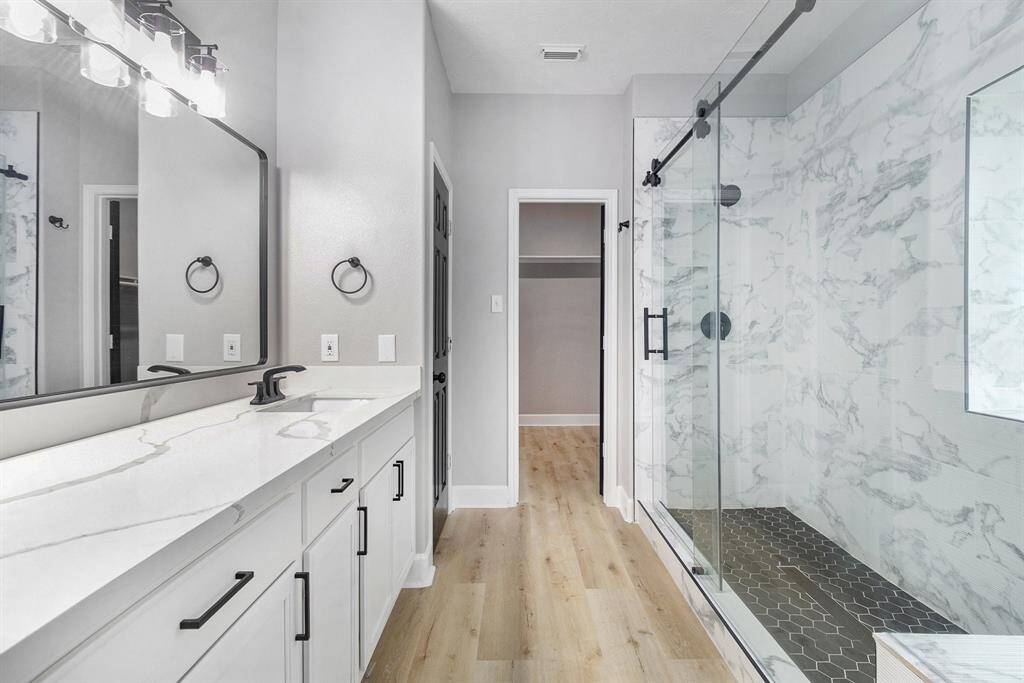 This bathroom features a sleek modern design with a spacious glass-enclosed shower, water closet, dual sinks with a large mirror, and stylish black fixtures.