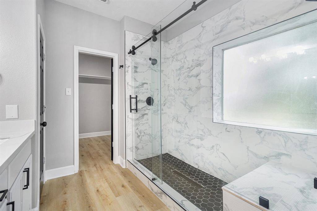 This bathroom features a sleek walk-in shower and a sliding glass door. There's a large frosted window for natural light and a doorway leading to a spacious closet.