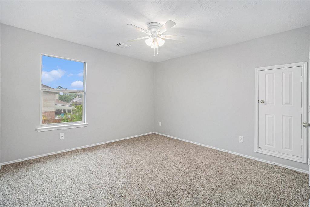 This secondary bedroom features soft gray walls, a plush carpet, and a ceiling fan with a light fixture.