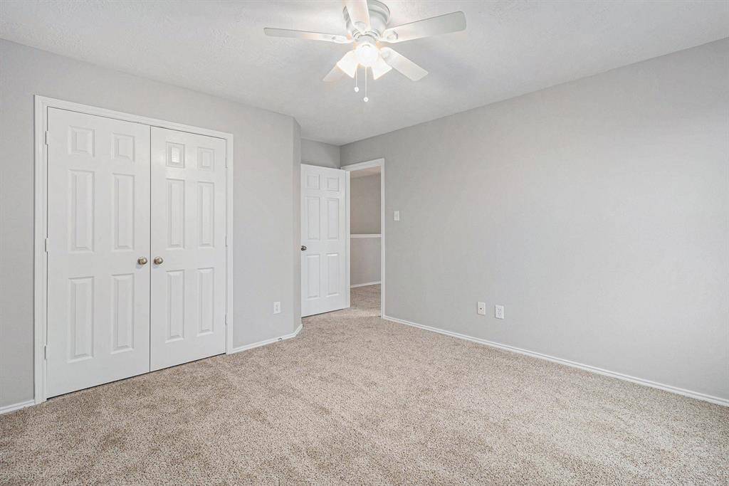 This secondary bedroom features soft carpeting, neutral gray walls, a ceiling fan, and ample natural light. It includes a spacious closet with double doors, offering functional storage space.