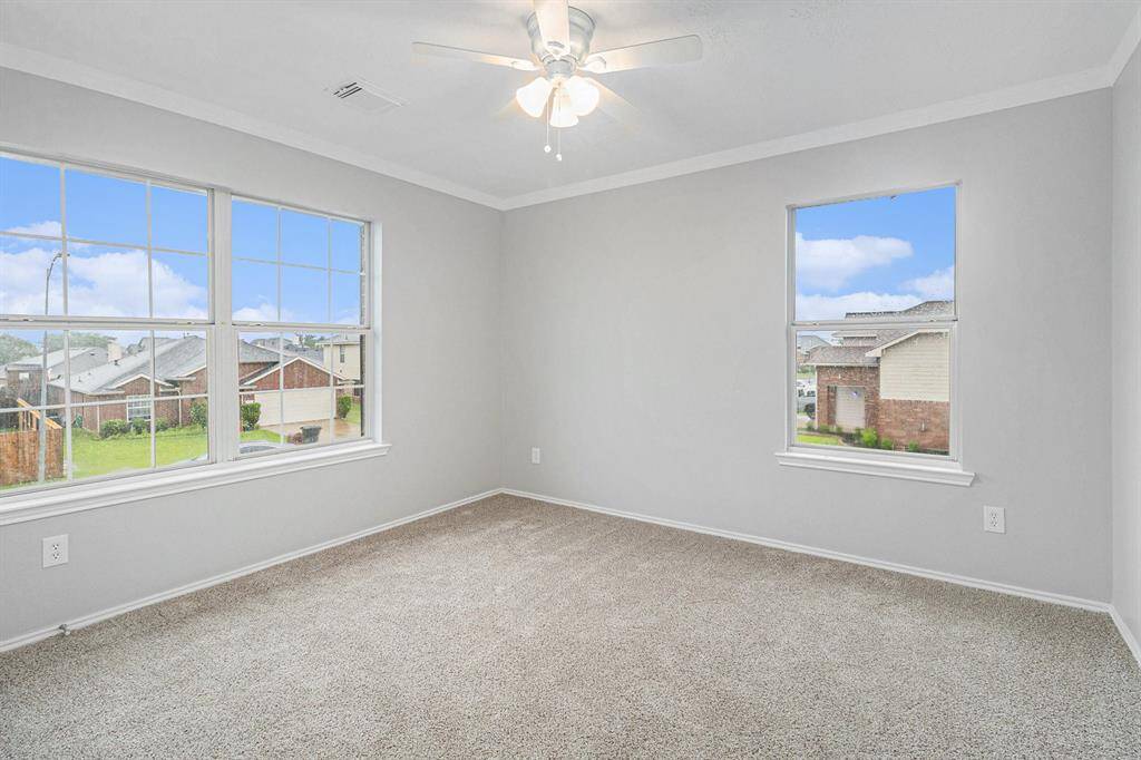 Bright, spacious secondary bedroom with neutral walls and carpeting, featuring large windows for natural light and a ceiling fan for comfort.