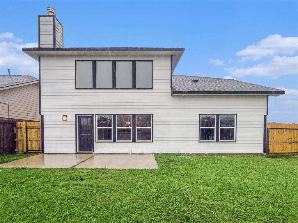 This photo showcases the back of a two-story house features white siding and large windows. It has a small concrete patio leading to a spacious, fenced backyard, perfect for outdoor activities.
