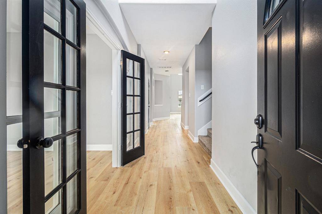 Bright entryway with new flooring and black-framed glass doors leading to an adjacent flex space. The hallway extends towards a staircase, creating an inviting and open feel.