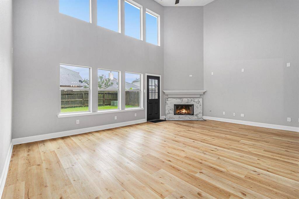 A spacious living room with high ceilings and abundant natural light from tall windows. It features new flooring, a modern fireplace and a neutral color palette, creating a warm and inviting atmosphere.