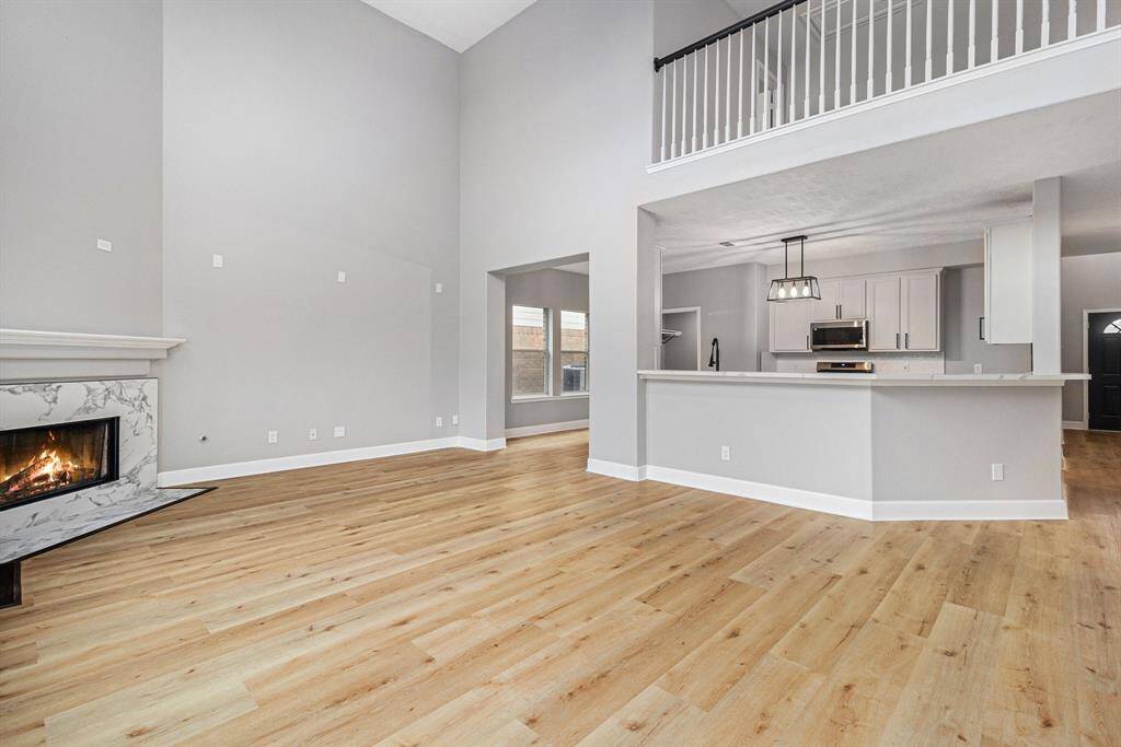 This spacious open-concept living area features high ceilings, a modern kitchen with stainless steel appliances, and a cozy fireplace. T