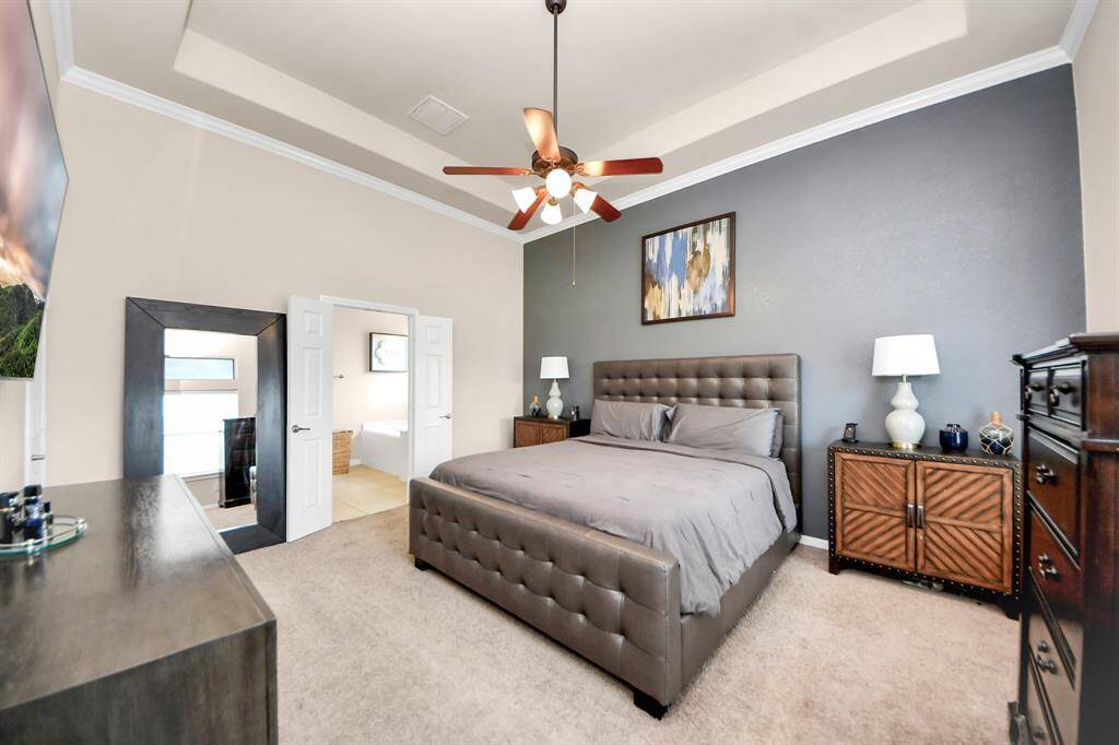 The primary bedroom has a feature wall, tray ceilings adorned with a ceiling fan.