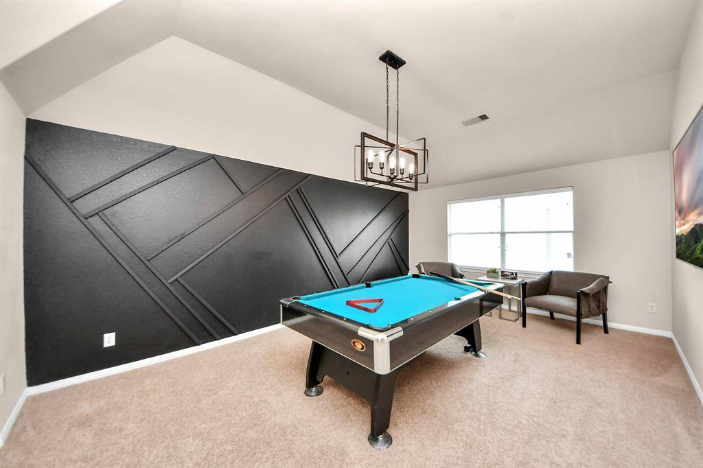 The game room includes a feature wall, high ceilings, and chandelier.