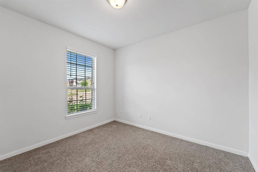 This light-filled home office offers a peaceful workspace with a front-facing window and soft carpet underfoot.