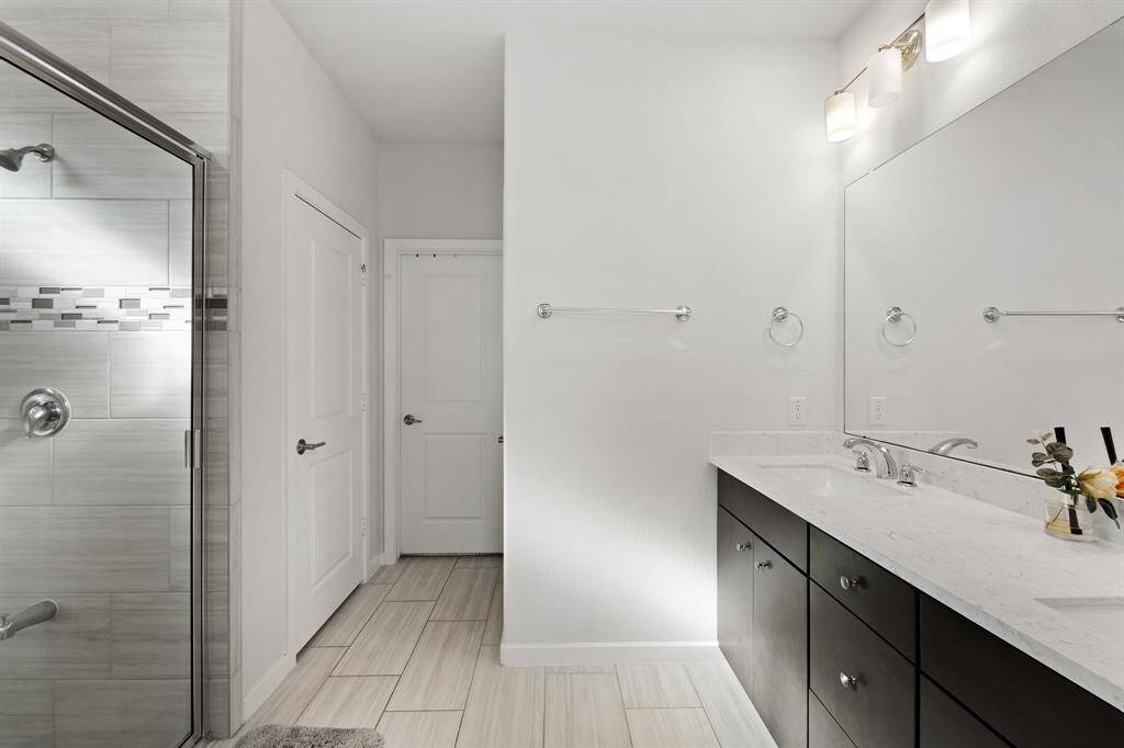 The ensuite bathroom boasts a dual-sink vanity with elegant countertops and modern fixtures, just steps away from the glass-enclosed walk-in shower.