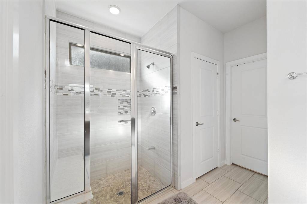 A sleek walk-in shower features floor-to-ceiling tilework, decorative accent trim, and a bench ledge for comfort and convenience.