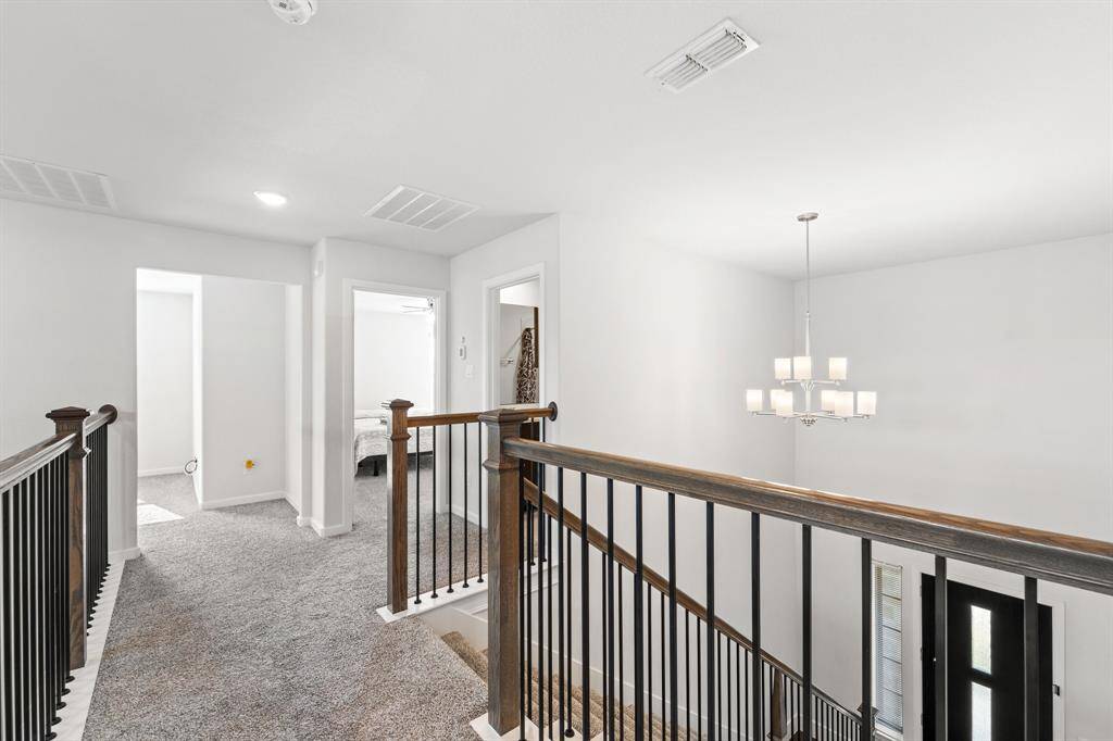 Spacious upstairs landing features iron spindles, wood-accented railing, and access to all secondary bedrooms and bathrooms. Natural light and a modern chandelier complete the open and airy feel.