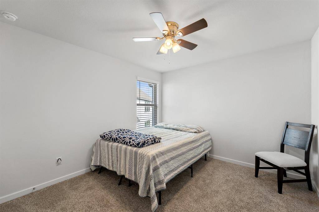 Cozy secondary bedroom with soft carpeting, neutral tones, and natural light pouring in through a window.