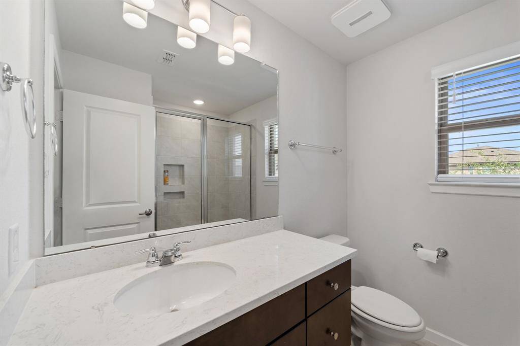 Full bathroom featuring a sleek vanity, walk-in shower with built-in shelves, and a window for added light.