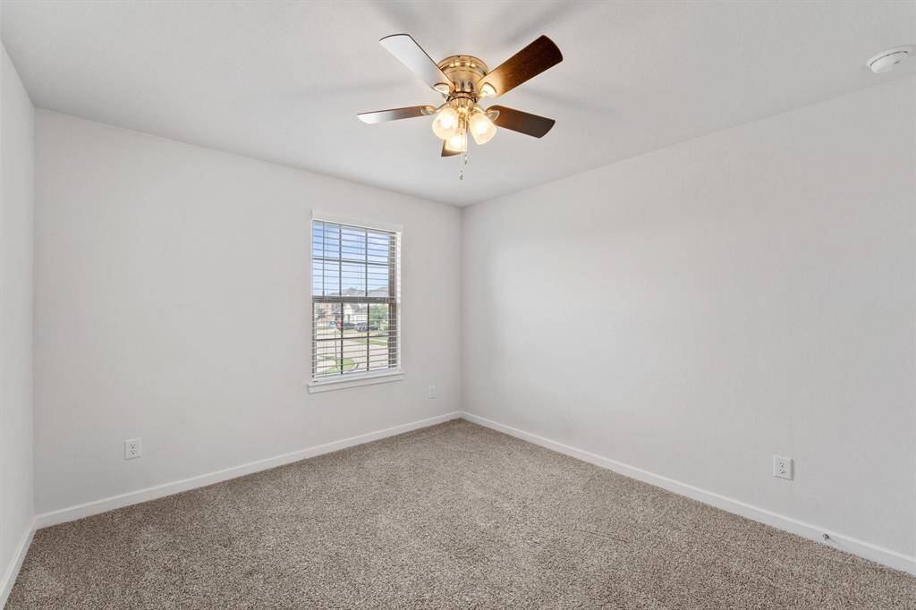 Bright secondary bedroom with plush carpet, ceiling fan, and a large window overlooking the front yard.