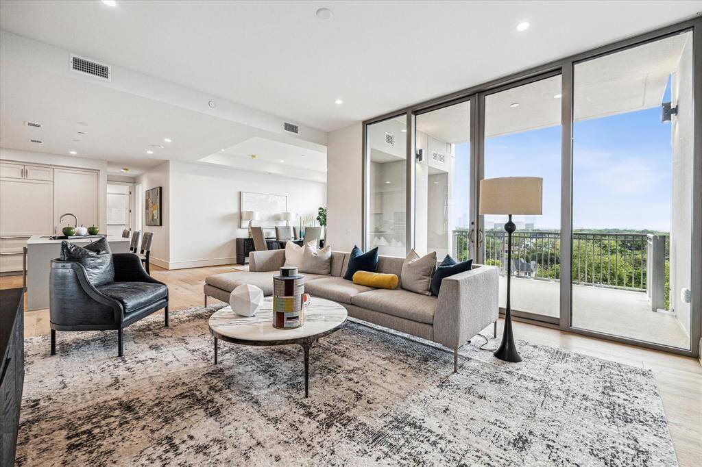 Open living space with expansive floor-to-ceiling windows, providing abundant natural light and sweeping views of the city. The spacious layout features clean architectural lines, recessed lighting, and direct access to a private balcony.