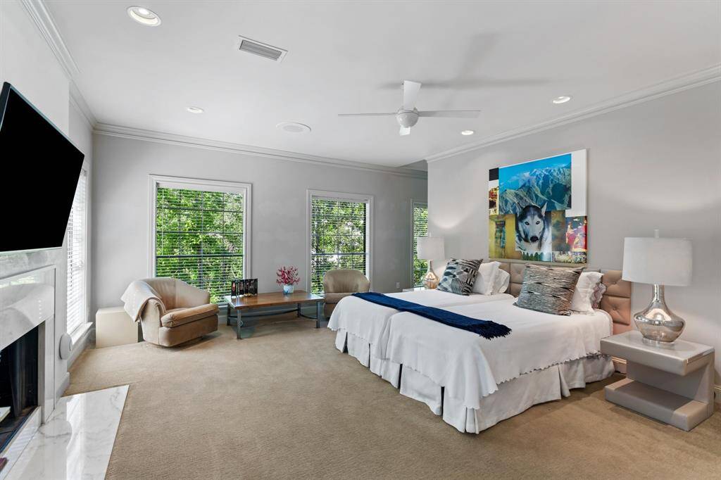 A view of the Primary Bedroom showing the fireplace wall, ceiling fan, and windows facing north and west for natural light.