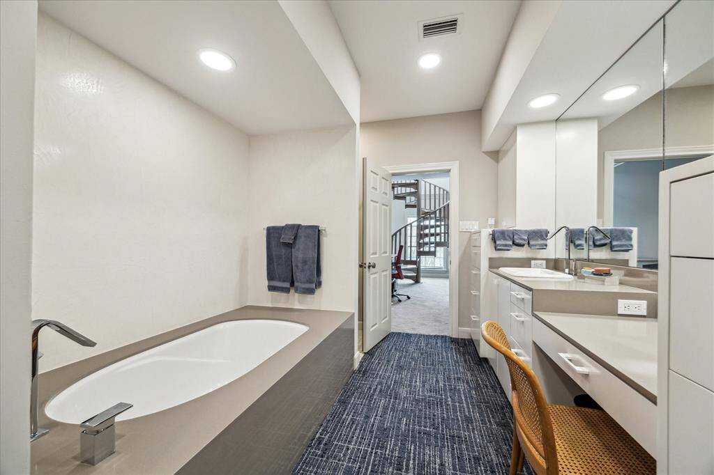 One of two Primary Bath vanities with Silestone vanity, counter to ceiling mirrors, recessed lighting, and makeup knee space. Alternate angle showing the vanity and deep soaking tub, surrounded by elegant tile and ample natural light.