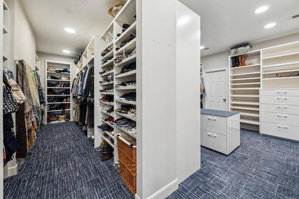 One of two expansive, custom walk-in closets in the Primary Suite with custom shelves, valet bars, and a packing island  with drawers below.