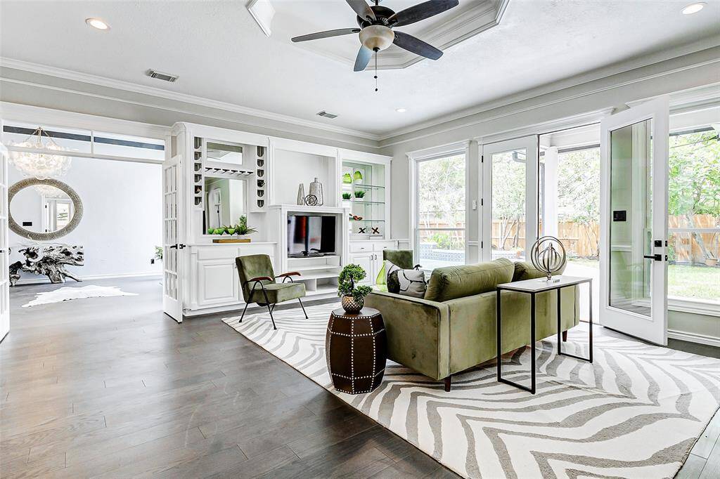 The inviting living room features an open layout with large windows and French doors leading to a backyard, offering abundant natural light. It includes a modern ceiling fan, built-in shelving, and a cozy seating area ideal for relaxation and entertaining.