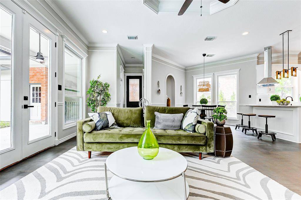 Bright, open living area with a modern design. Large windows for natural light, and a spacious kitchen with an island and bar stools. The room is elegantly decorated with a neutral palette and contemporary lighting fixtures.