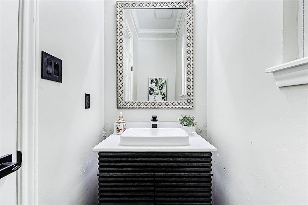 The guest half bathroom is located off the side entrance by the breakfast area. It features a stylish quartz vanity with a contemporary sink, a large decorative mirror, and minimalist decor, creating a clean and elegant look.