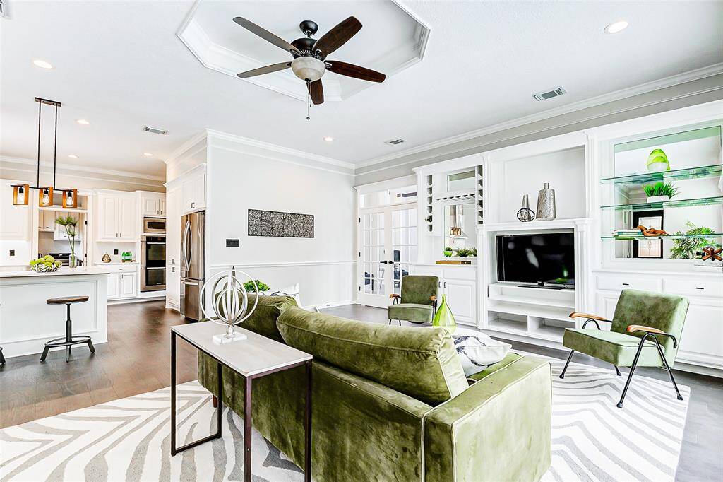 This modern living area features an open floor plan with a stylish kitchen, complete with a breakfast bar and pendant lighting. The space is bright and airy, with white cabinetry and built-in shelves.A ceiling fan and recessed lighting add to the comfort and functionality.