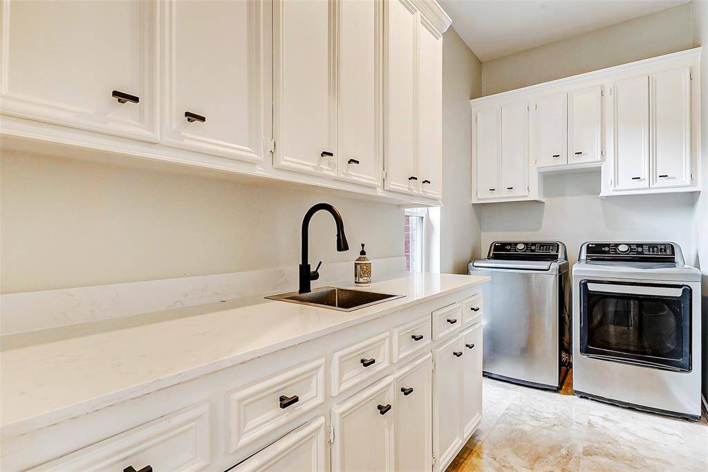 The spacious laundry room is located off the kitchen and features ample storage space, a modern black faucet, and stainless steel utility sink.