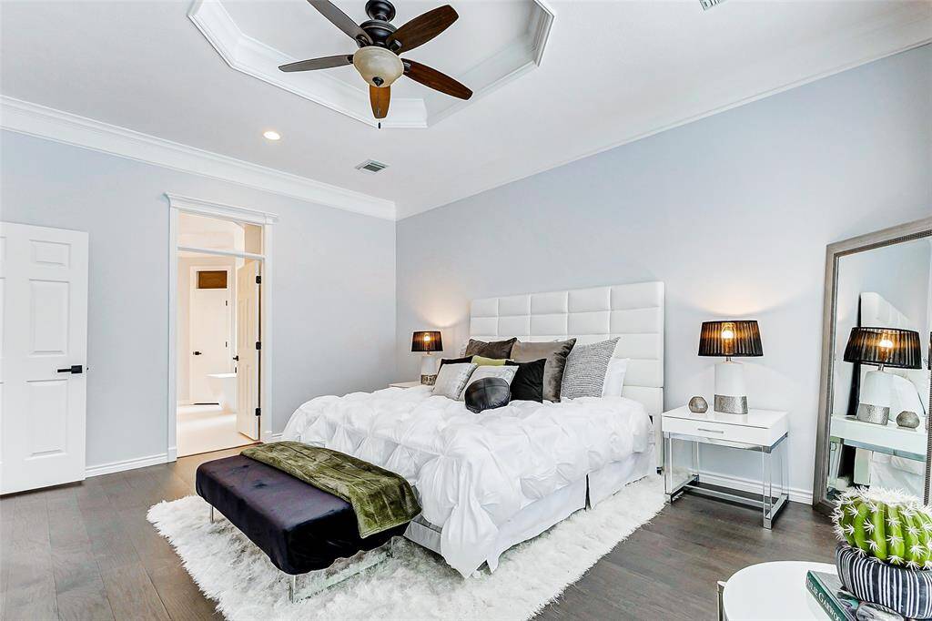 This spacious bedroom is accented with dark engineered wood flooring, and soft, neutral wall colors, creating a serene and inviting atmosphere.