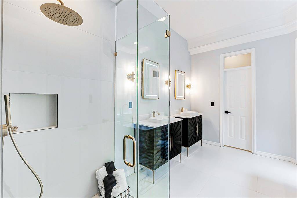 The en-suite bathroom features a large frameless shower, dual sinks with sleek black vanities, and elegant lighting fixtures for a bright and contemporary feel.