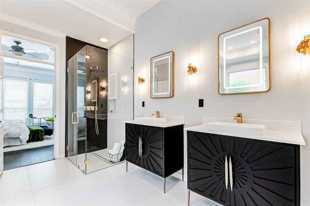 This luxury bathroom showcases an exquisite design with dual vanities with stylish black cabinets. It is well-lit with contemporary lighting fixtures and flows seamlessly onto the primary bedroom.