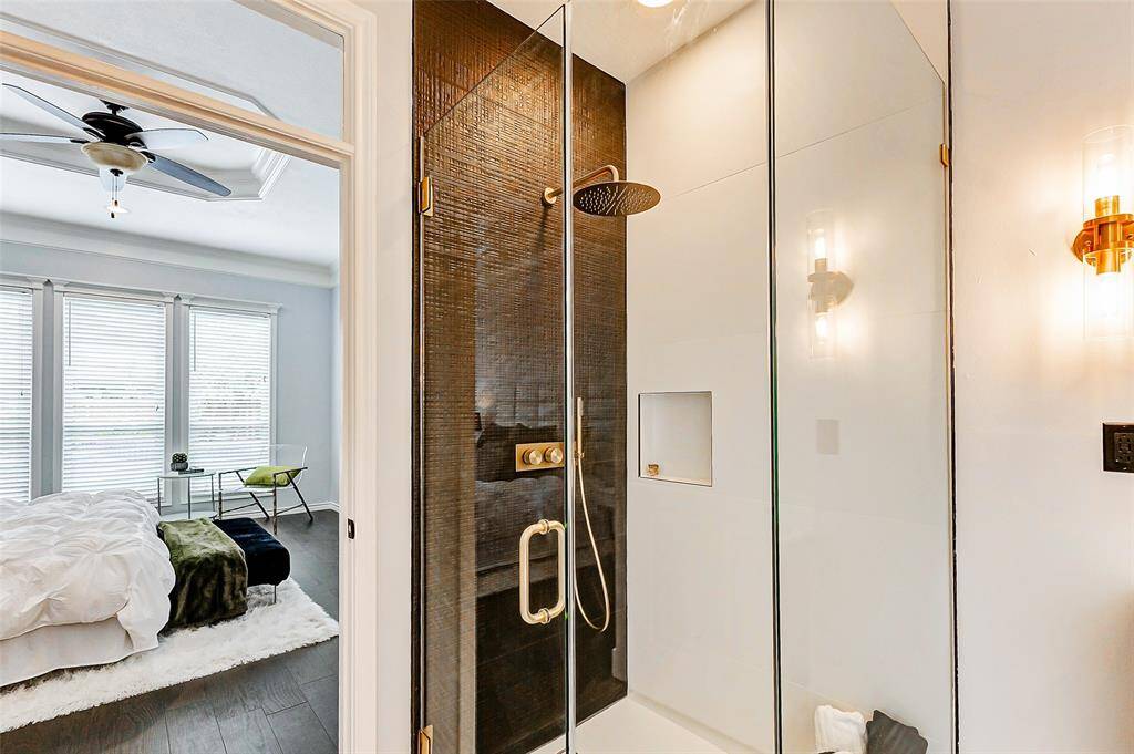 The frameless glass-enclosed shower spotlights elegant black tiling and gold fixtures.