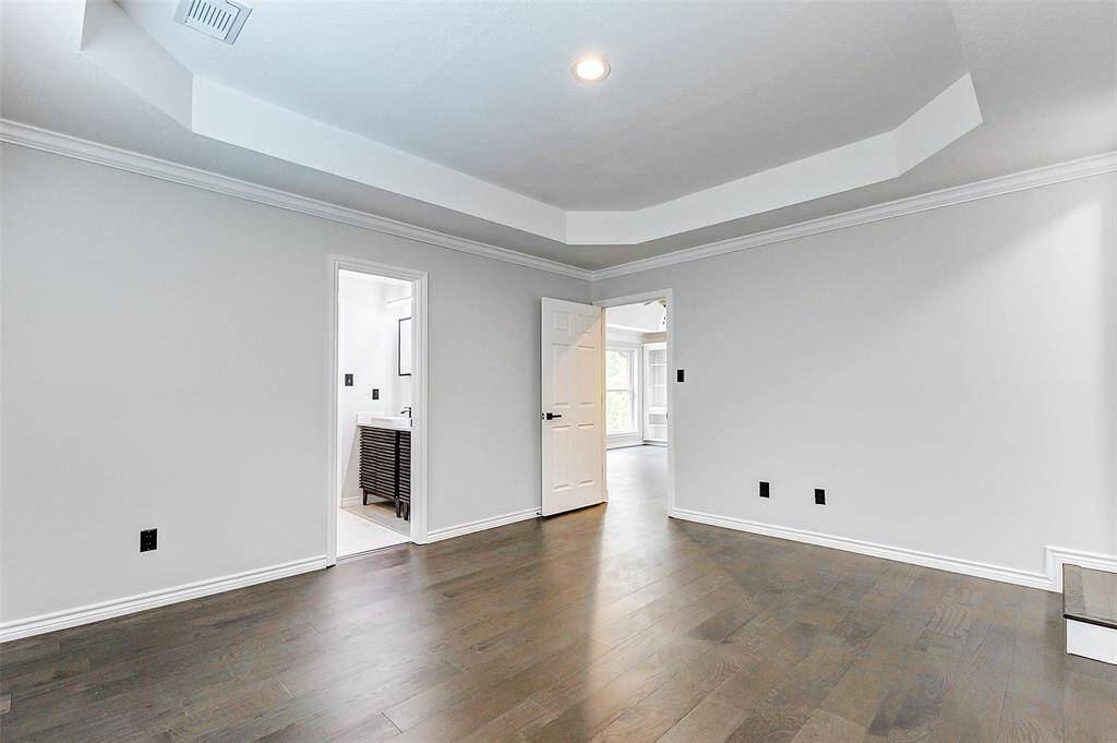 The 1st of the three secondary bedrooms located upstairs with engineered wood floors, neutral gray walls, and a recessed ceiling with crown molding. It features a doorway leading to a Jack & Jill bathroom.