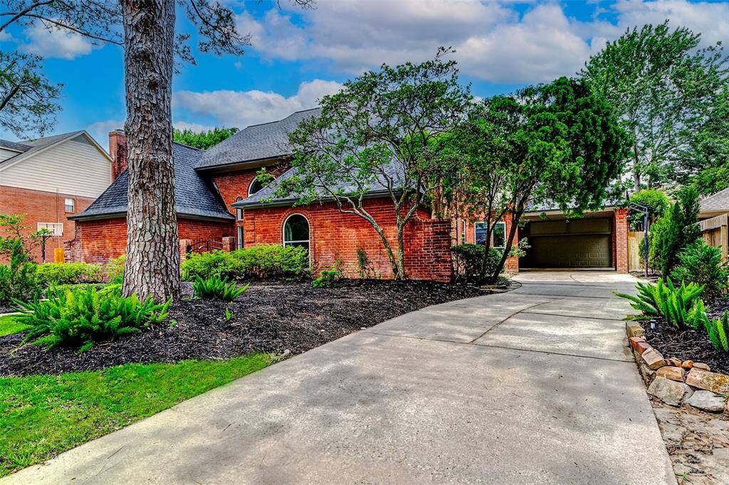 Lovely brick home with a well-maintained front yard featuring lush greenery and mature trees. The property includes a spacious driveway leading to a covered garage, offering plenty of parking space.