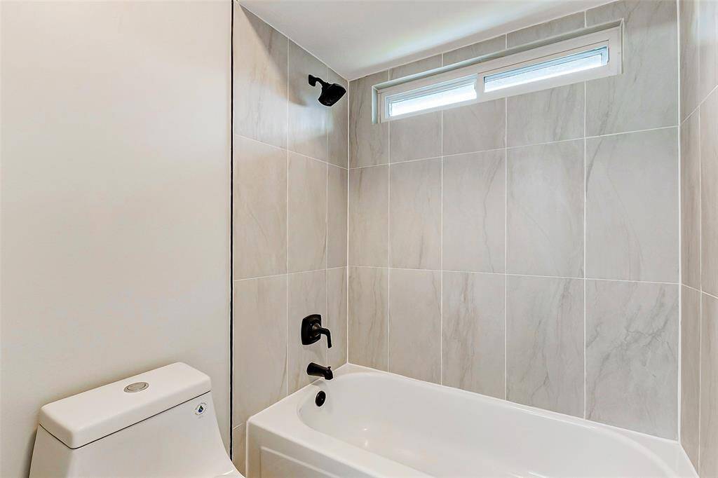 The Jack & Jill bathroom features a sleek white bathtub with dark fixtures, complemented by a tiled shower and a narrow horizontal window for natural light.