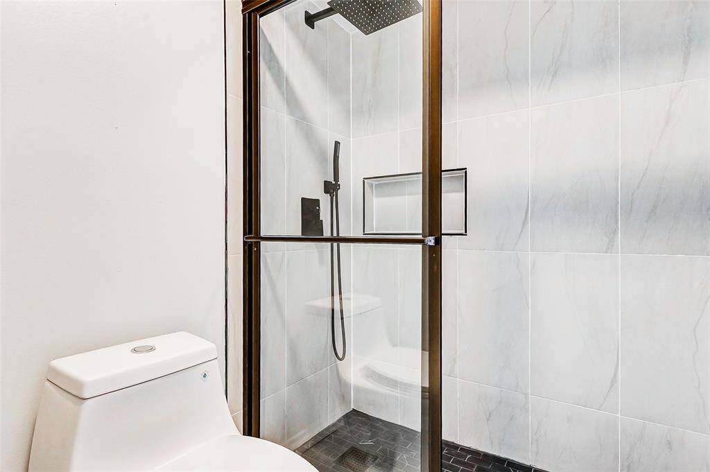 This bathroom showcases a modern shower with a sliding glass door, rainfall shower head, and built-in niche. It has sleek white tiles and a compact toilet, creating a clean, contemporary look.
