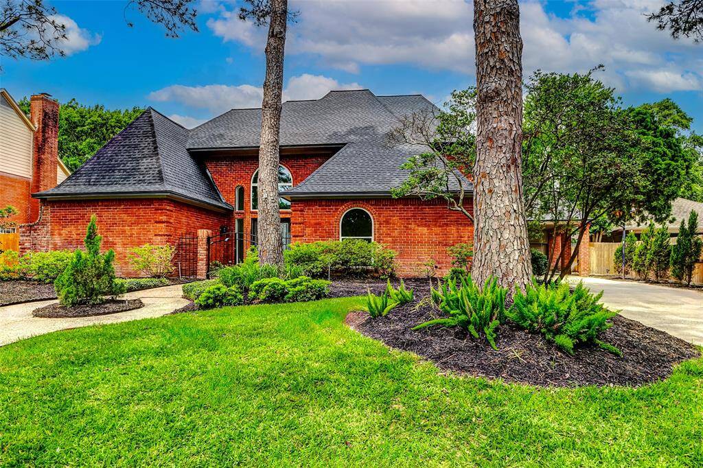Charming brick home with a new dark shingled roof, set amidst lush landscaping. The front yard features mature trees and well-maintained shrubs, offering great curb appeal.