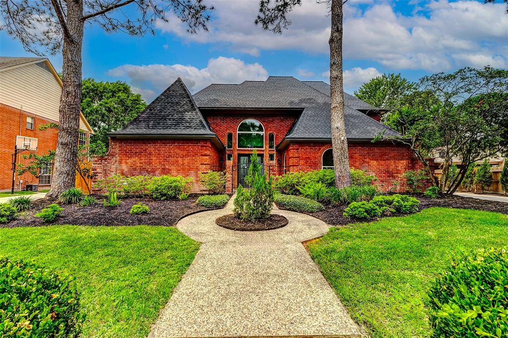 The home features a distinctive roofline and a brick elevation with inviting arched entryway, surrounded by well-maintained landscaping and mature trees.