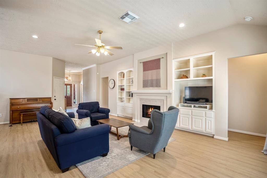 From this angle in the living room, you can see across the open layout toward the front door, with the garage entry conveniently tucked to the left. The doorways flanking the fireplace lead to the secondary bedrooms on the left and the private primary suite on the right. Don’t miss the beautiful built-ins that frame the fireplace, adding both function and character.