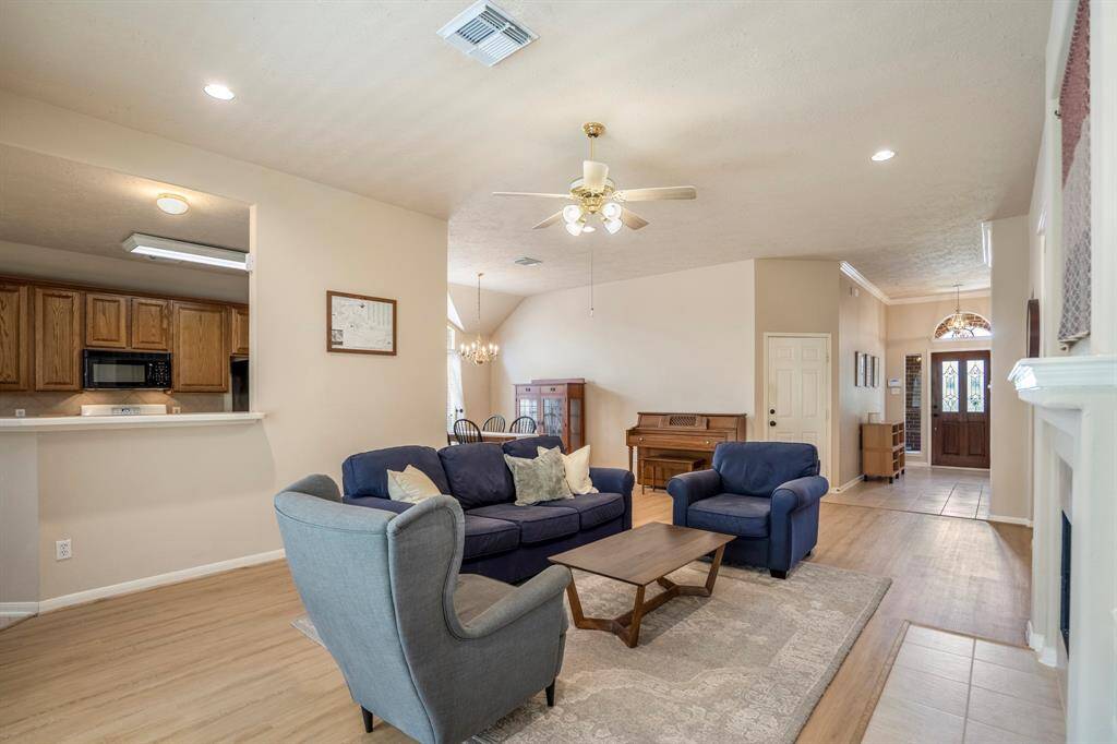 Moving back into the living area from the primary suite, the kitchen is visible across the breakfast bar on the left. Looking ahead, you can see the formal dining area, and to the right, the open space leads toward the front door, showcasing the home's seamless flow and openness.