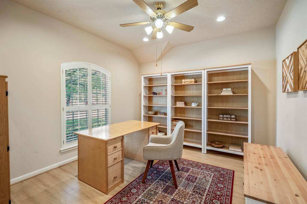 A peek inside the study reveals brand new vinyl plank flooring, vaulted ceilings with recessed lighting and a ceiling fan, and plantation shutters that frame the view of the front yard.