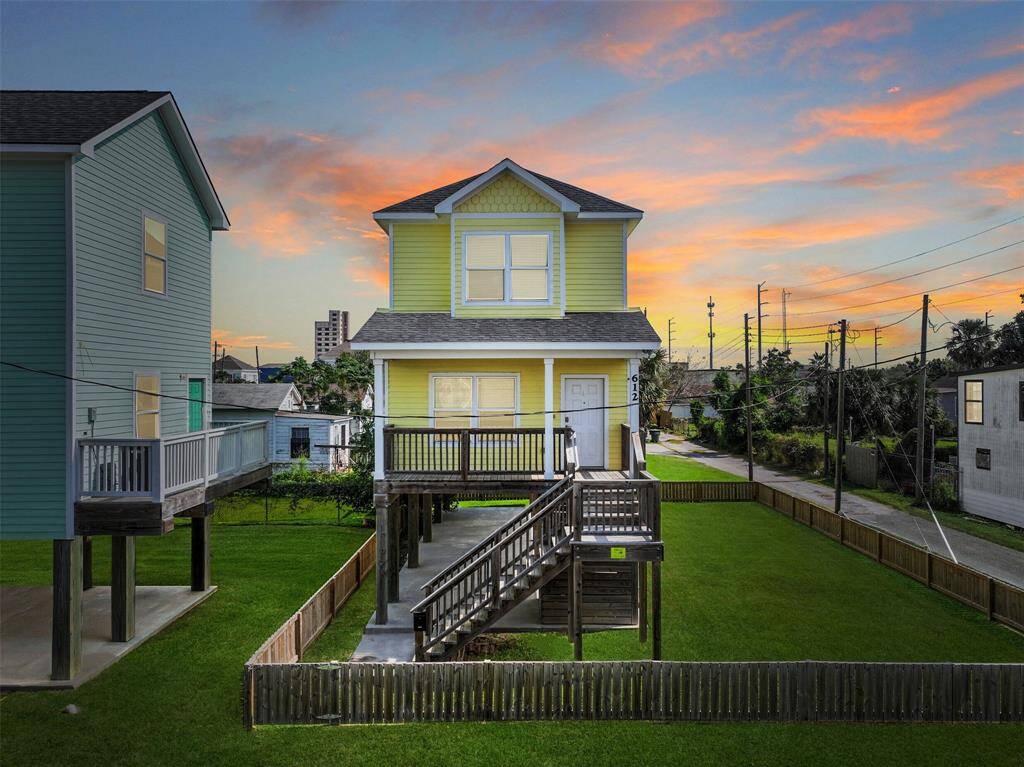 This charming two-story home features a vibrant yellow exterior with a spacious front porch and elevated entrance. The property includes a well-maintained lawn surrounded by a wooden fence, offering a cozy backyard space. The neighboring lot (included in the fenced area) is also for sale separately!