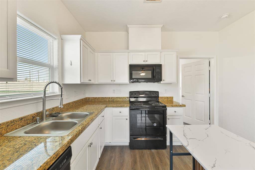 Enter the light & bright kitchen with modern black appliances, white cabinetry, granite countertops, and a moveable central island with a marble-inspired countertop. Luxury vinyl plank flooring adds warmth & functionality.