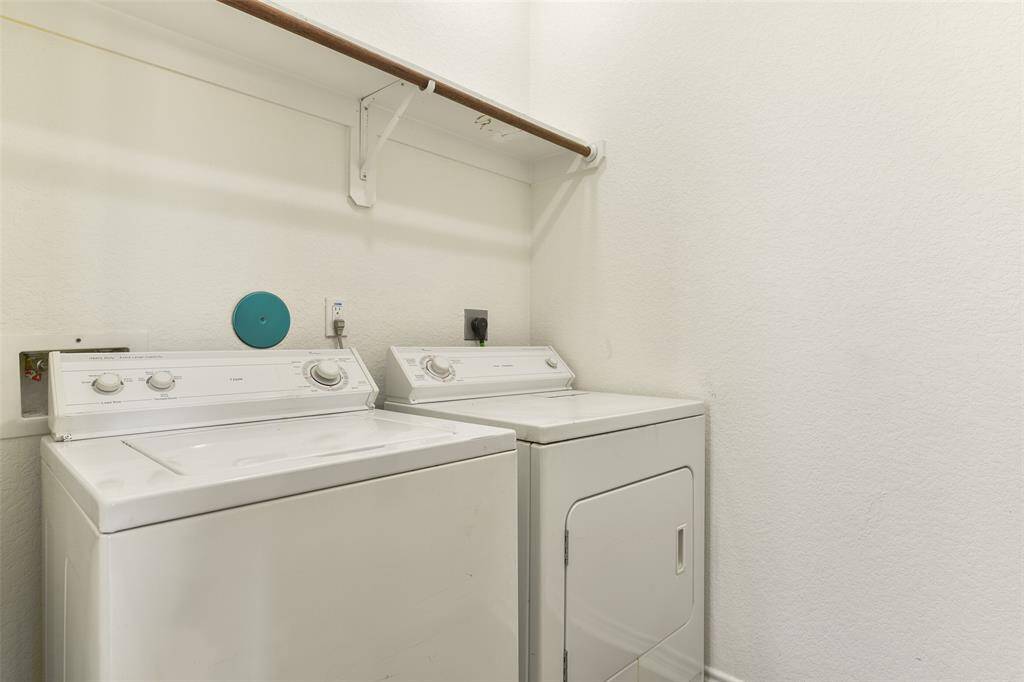 This photo highlights a compact laundry room with a washer and dryer side by side, a shelf above for storage, and neutral walls for a clean look.